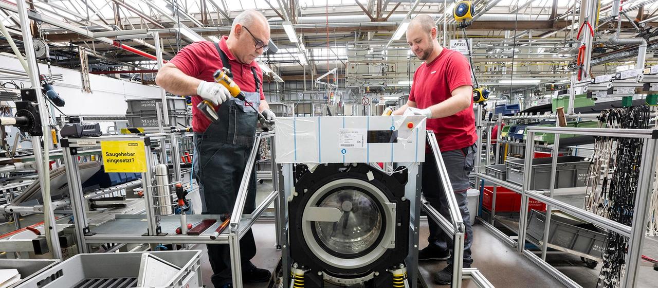 Mitarbeiter fertigen eine gewerbliche Waschmaschine in einer Produktionshalle.
