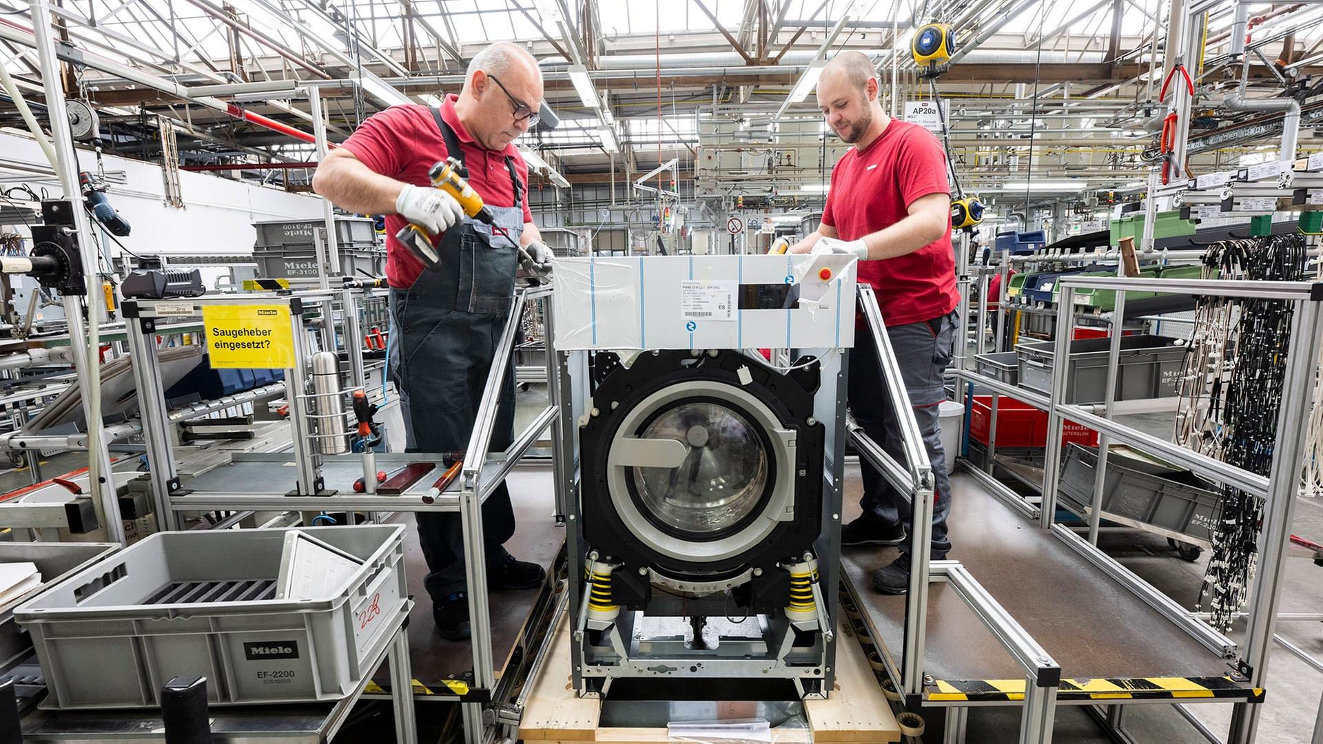 Mitarbeiter fertigen eine gewerbliche Waschmaschine in einer Produktionshalle. | picture alliance/dpa