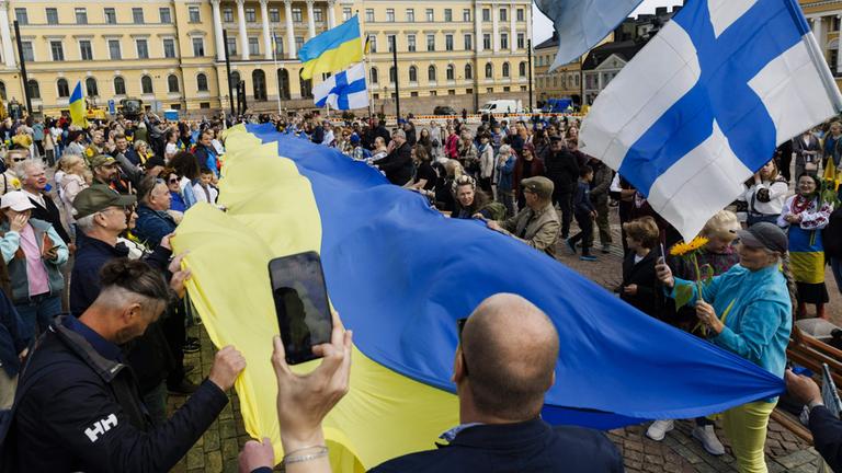 In Helsinki halten Menschen ukrainische und finnische Flaggen hoch.