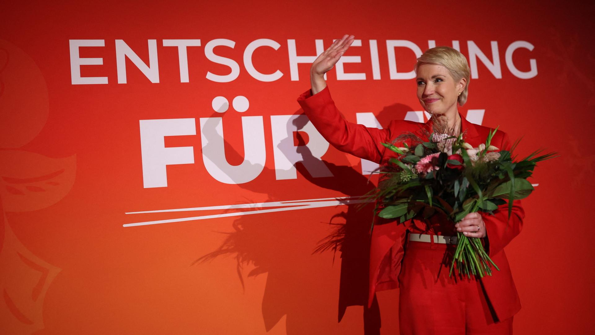 Manuela Schwesig winkt, in einer Hand hält sie einen Blumenstrauß. | AFP