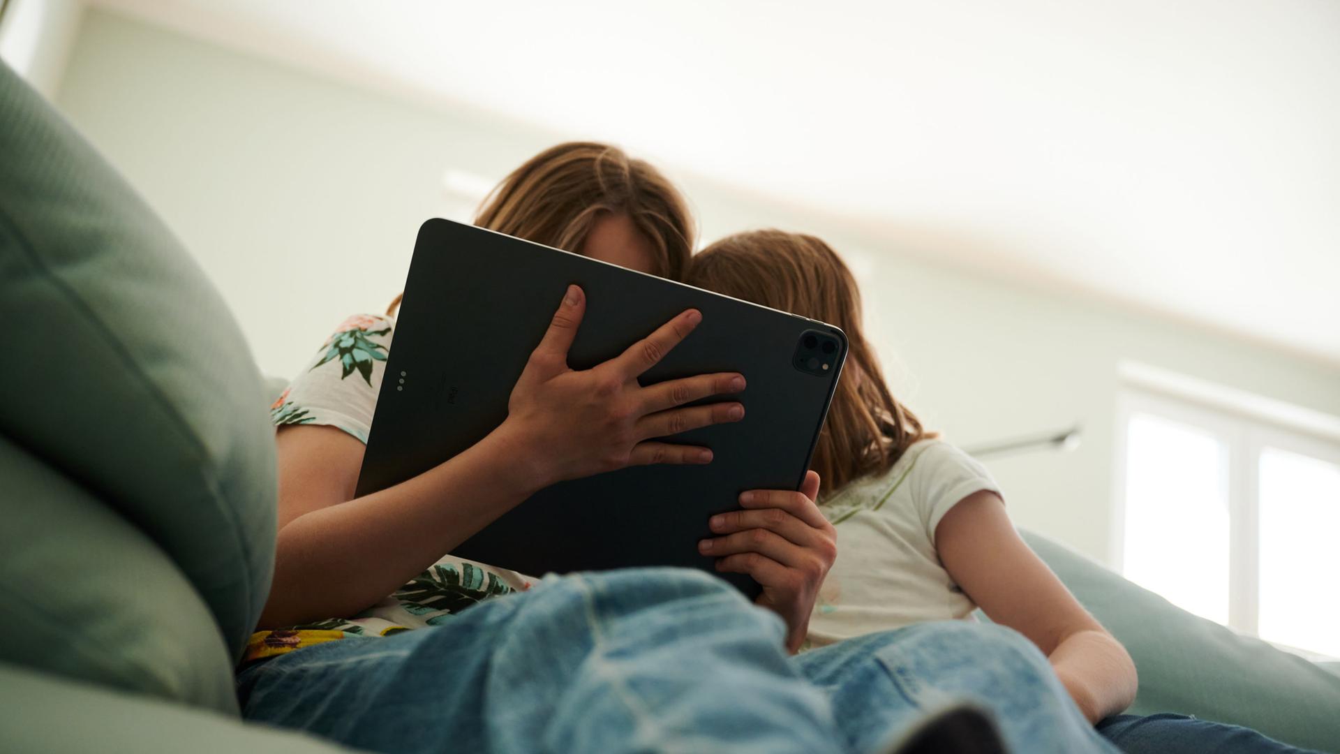 Zwei Schwestern sitzen auf der Couch und gucken in das Tablet ihrer Eltern. | dpa