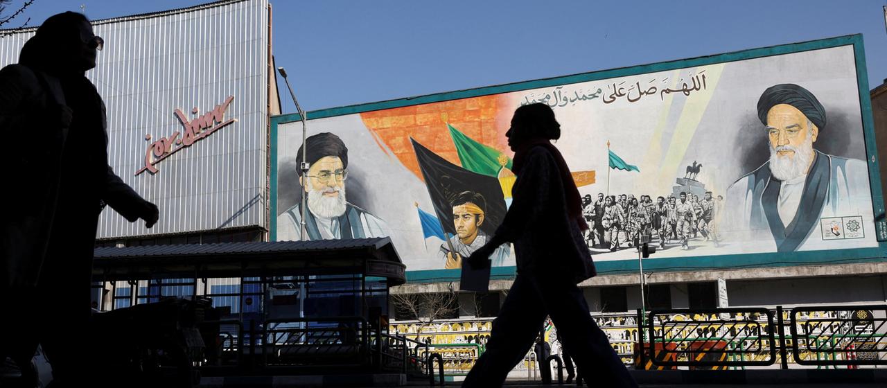 Menschen gehen in Teheran (Iran) an einem Wandgemälde vorbei, das Bilder von Ayatollah Ali Chamenei und Ayatollah Ruhollah Chomeini zeigt.