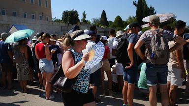 Touristen tragen Hüte und benutzen Fächer und Regenschirme um sich vor der Hitze zu schützen.