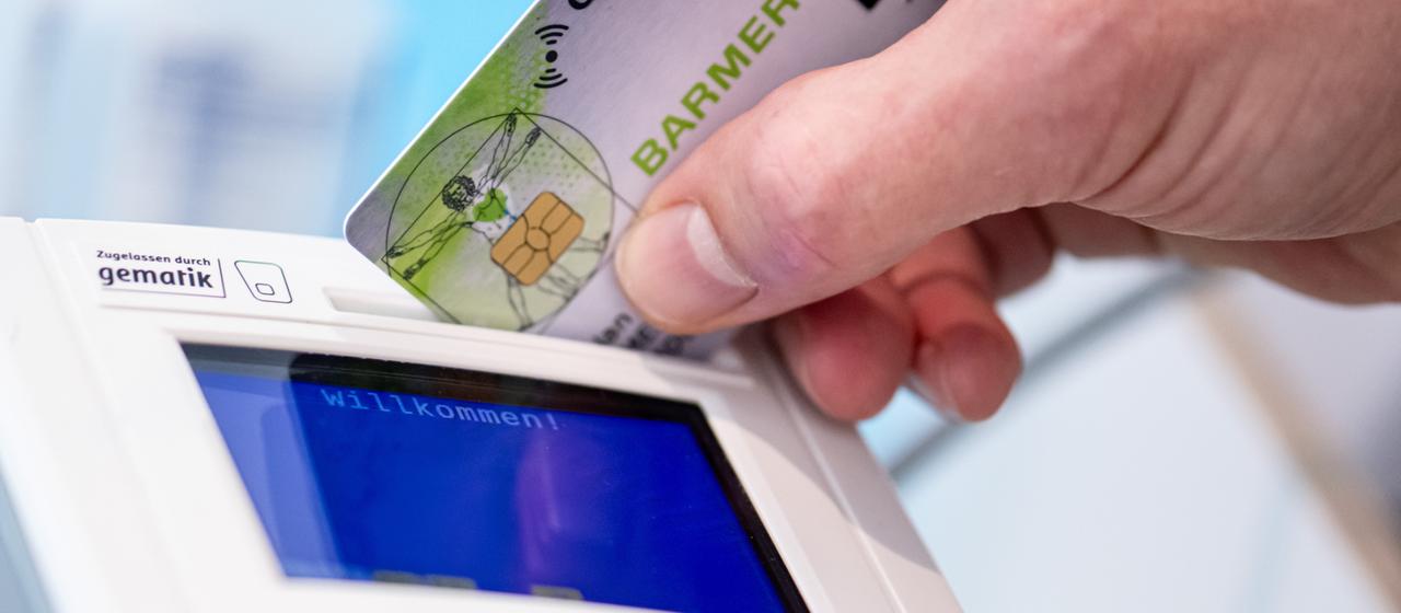 Eine Hand steckt eine Gesundheitskarte in ein Lesegerät.