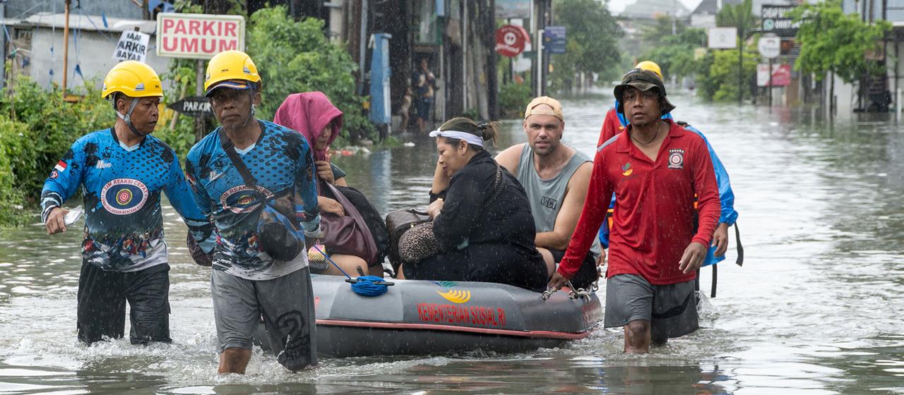 Eine Gruppe von Rettungskräften zieht ein Schlauchboot mit mehreren Personen durch eine überflutete Straße.