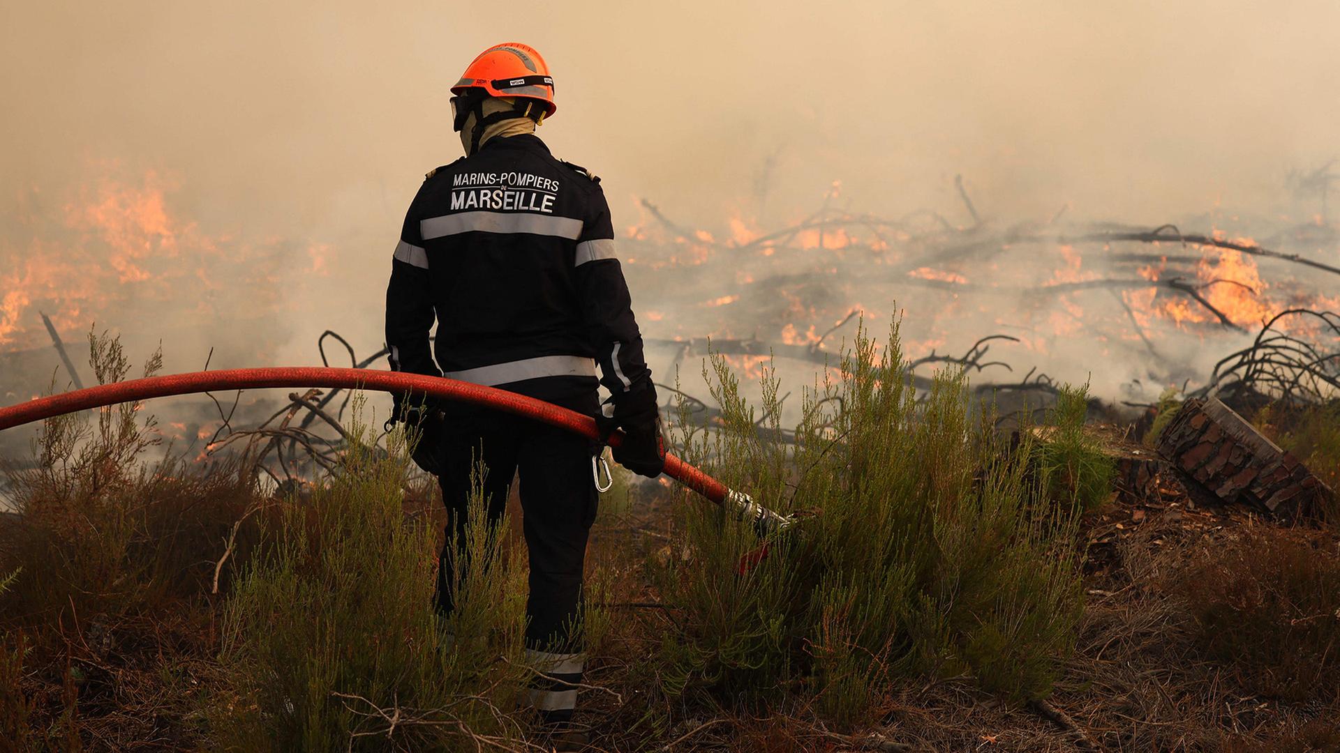 Ein Feuerwehrmann hält einen Schlauch in der Hand und beobachten die Flammen. | AFP
