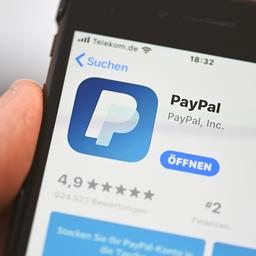 Die Applikation von PayPal ist auf einem Mobilfunkgerät zu sehen, das ein Mann in der Hand hält.