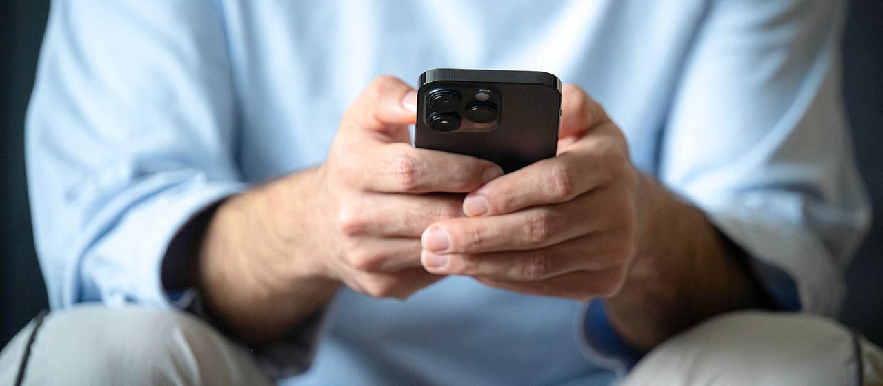 Ein Mann sitzt und schaut auf sein Handy.