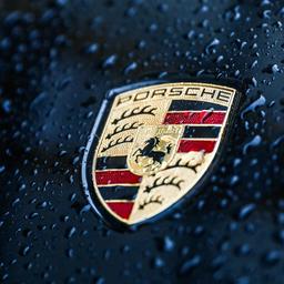 Porsche-Logo und Regentropfen auf einer Motorhaube.