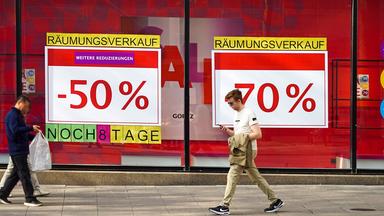 Passanten vor einem mit Räumungsverkaufs-Plakaten beklebten Schaufenster.