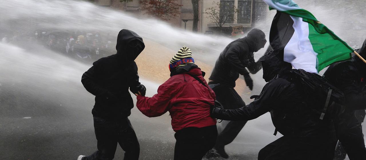 Demonstranten stehen im Strahl eines Wasserwerfers.