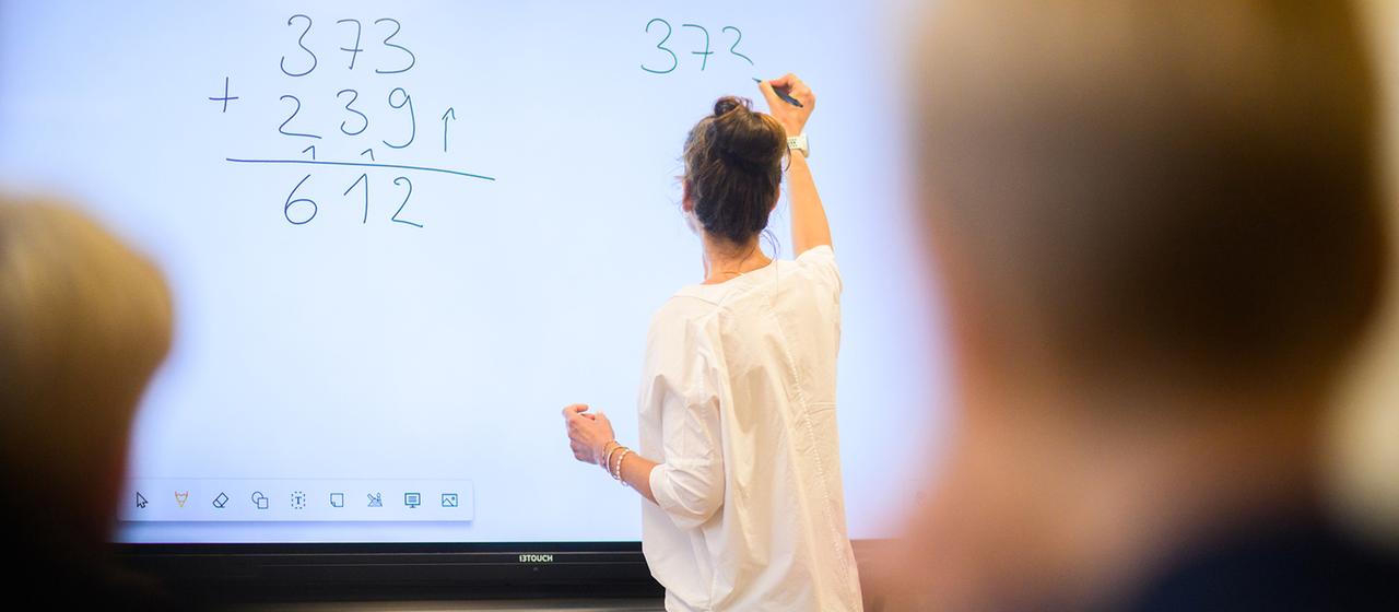 Eine Lehrerin schreibt eine Mathematikaufgabe auf eine digitale Schultafel im Klassenraum einer 4. Klasse einer Grundschule in der Region Hannover. 