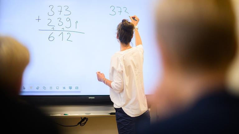 Eine Lehrerin schreibt eine Mathematikaufgabe auf eine digitale Schultafel im Klassenraum einer 4. Klasse einer Grundschule in der Region Hannover. 