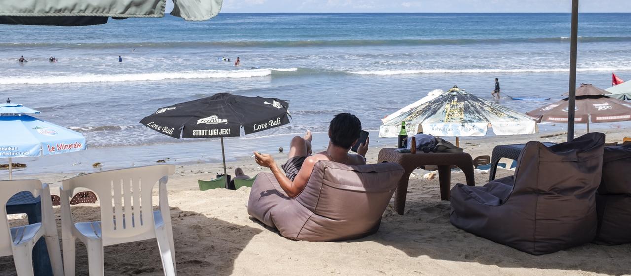 Ein ausländischer Tourist sitzt am Strand Kuta Beach in Bali.