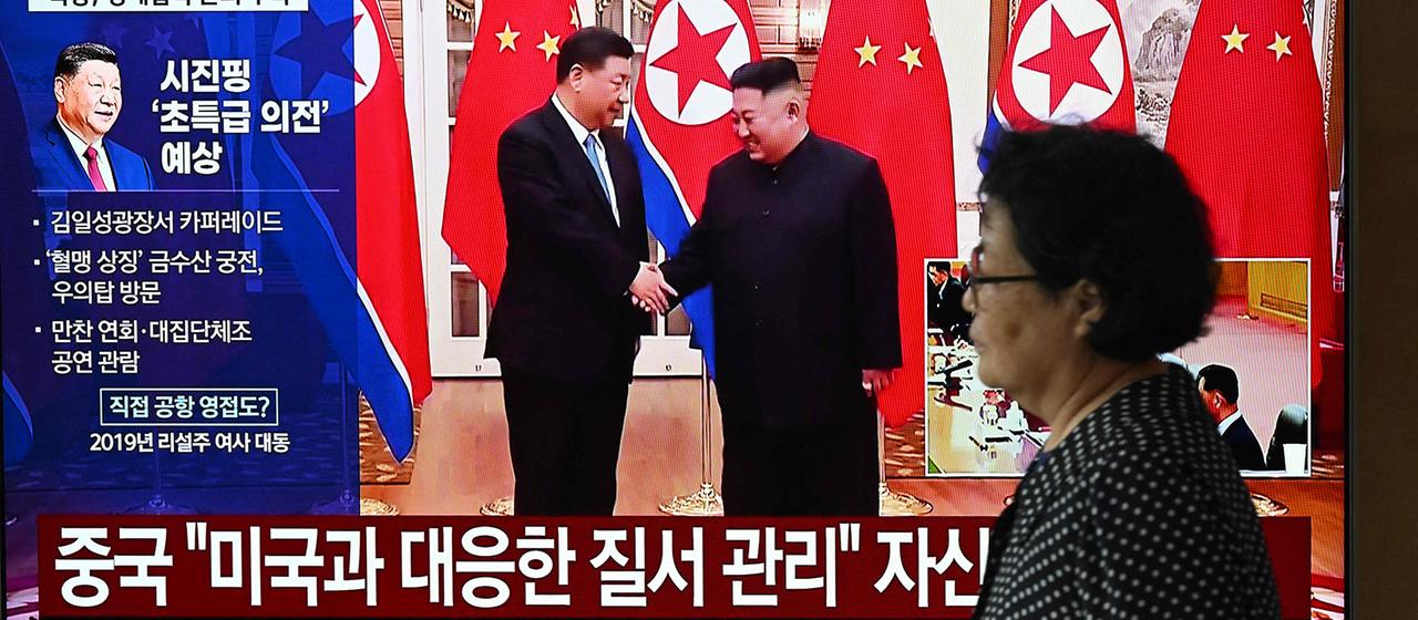 Ein Passantin in Seoul vor einem Bildschirm, der  Xi Jinping und Kim Jong Un zeigt.