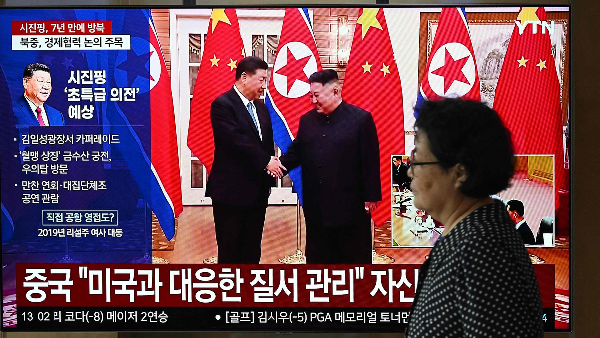 Ein Passantin in Seoul vor einem Bildschirm, der  Xi Jinping und Kim Jong Un zeigt. | AFP