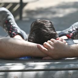 Ein Arbeiter legt auf einer Holzliege, die auf dem Rathenauplatz in der Frankfurt Innenstadt unter einem Schatten spendenden Baum platziert ist, eine Pause ein.