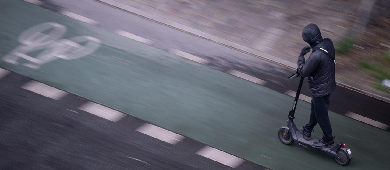 Ein Mann fährt mit einem E-Scooter auf einem Fahrradweg.