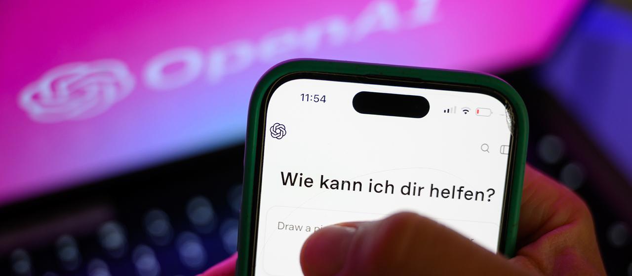 Ein Smartphone mit dem KI-Chatbot ChatGPT ist vor dem Logo des US-Softwareunternehmens OpenAI zu sehen. 