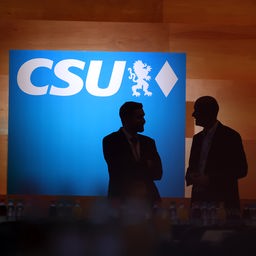 Besucher des CSU-Parteitags stehen vor dem CSU-Logo.