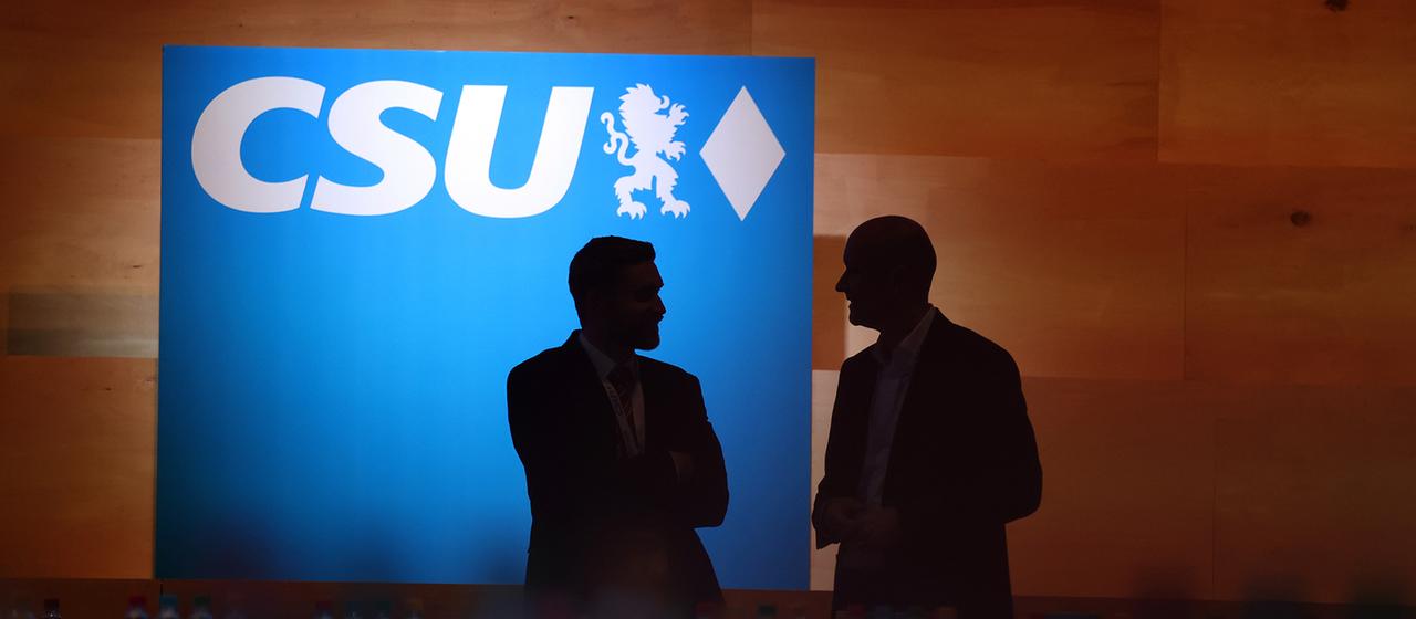Besucher des CSU-Parteitags stehen vor dem CSU-Logo.