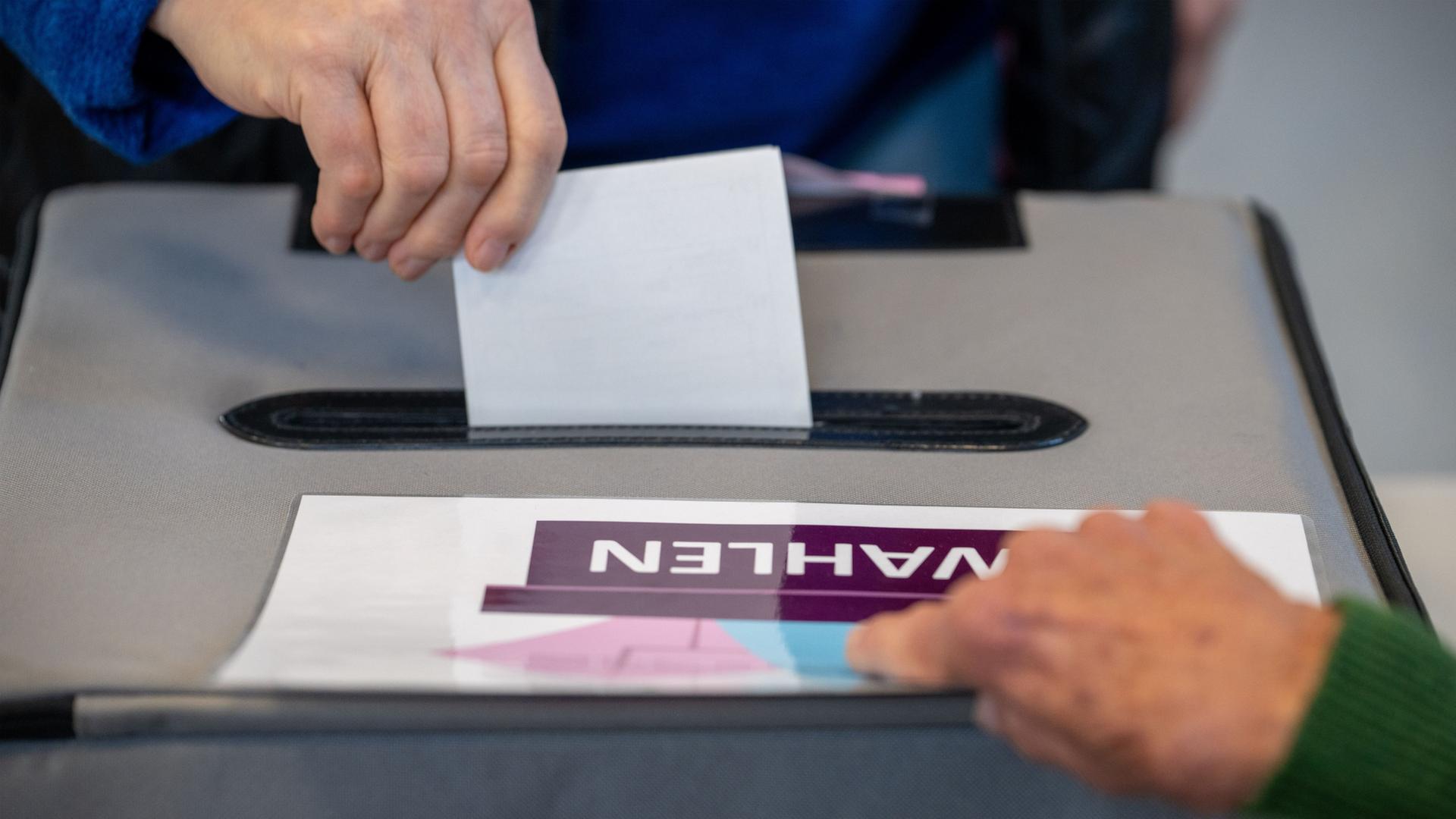 Jemand wirft seinen Stimmzettel in eine Urnenbox. | Harald Tittel/dpa