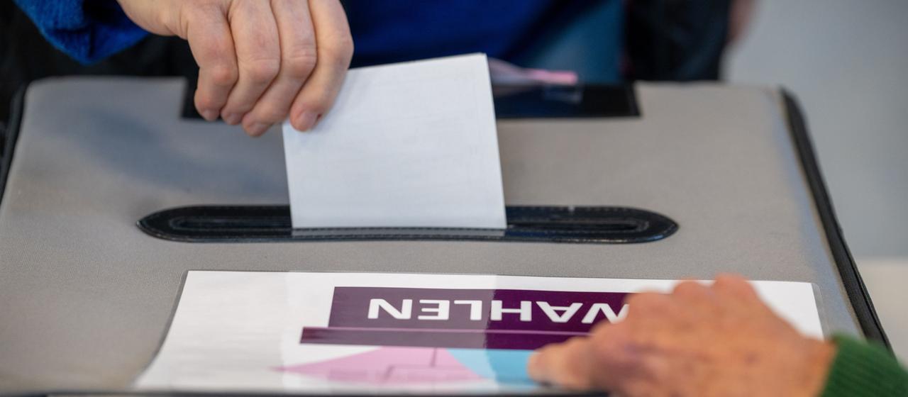 Jemand wirft seinen Stimmzettel in eine Urnenbox.