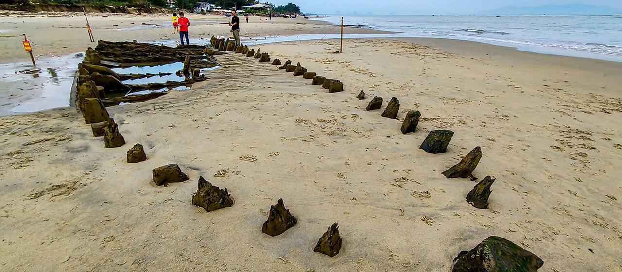 Menschen untersuchen das hölzerne Wrack eines Schiffes am Strand.