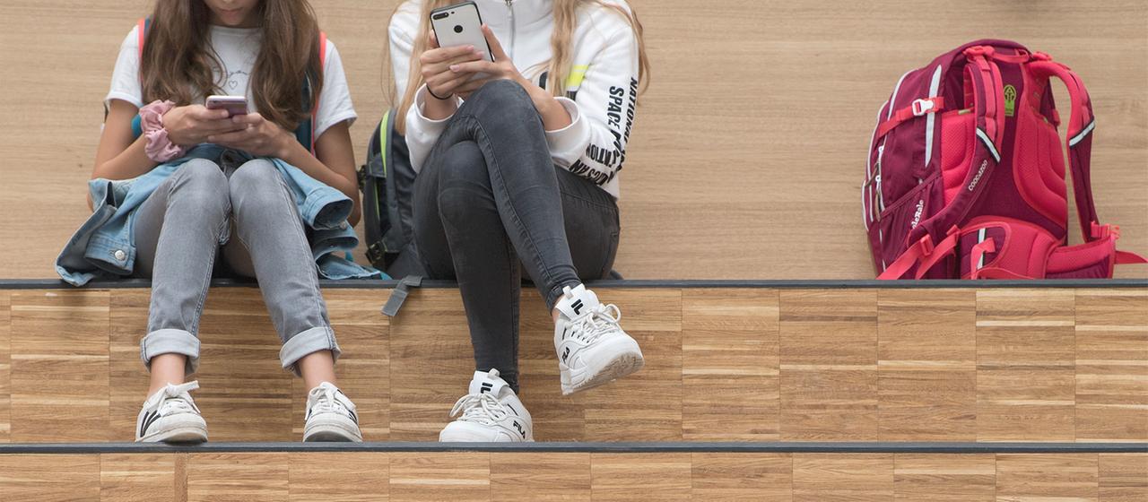 Girls sit on a step and hold smartphones in their hands. (Archive image from September 12, 2019)