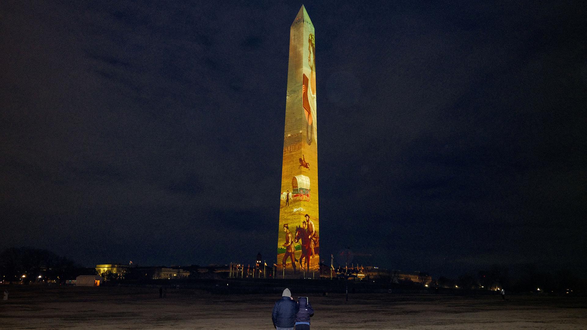 Menschen betrachten das Washington Monument, auf das Bilder und Videos projiziert werden. | REUTERS