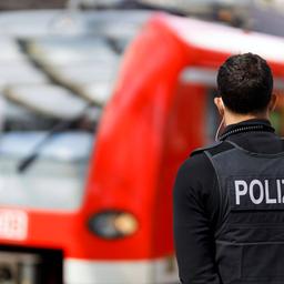 Ein Bundespolizist steht vor einem roten Zug an einem Bahngleis.