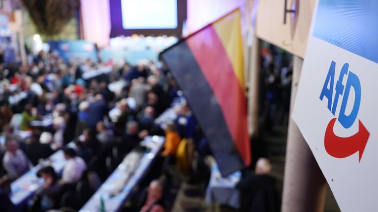 Ein Logo der AfD hängt neben eine Deutschlandfahne