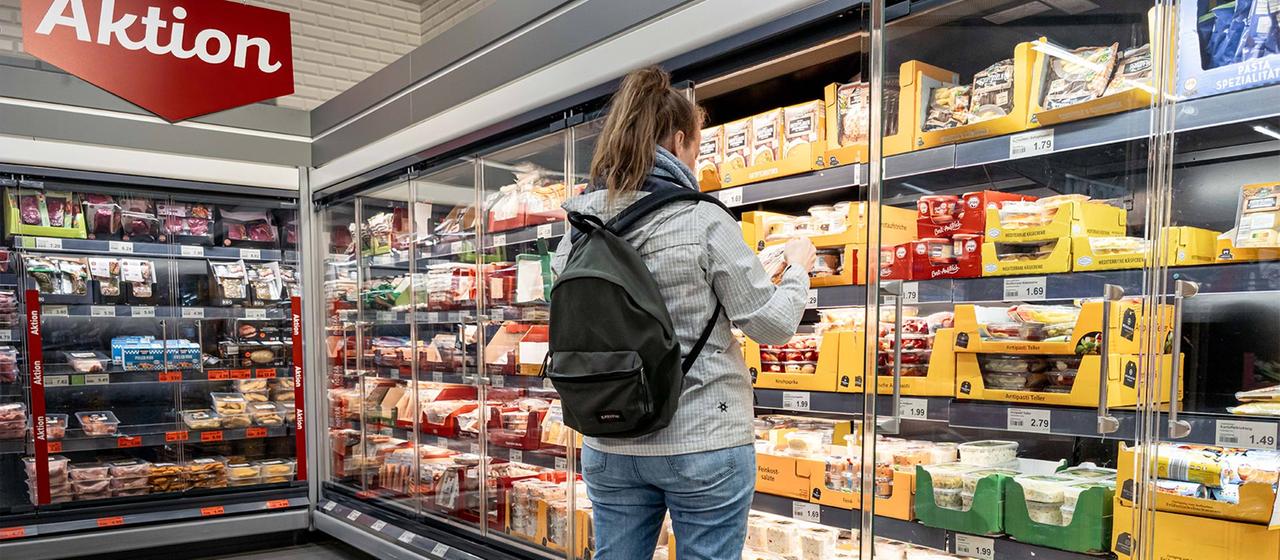 Eine Kundin steht in einem Supermarkt vor dem Kühlregeal.