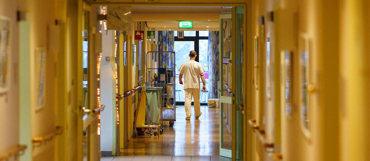 Ein Pfleger geht einen Gang eines Alten- und Pflegeheims entlang.