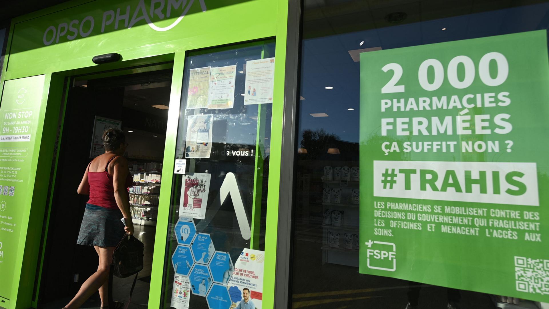 Eine Person betritt eine Apotheke in Frankreich. Dort steht ein Schild mit der Aufschrift „2000 Apotheken geschlossen, das reicht doch, oder? – Verraten“.  | AFP