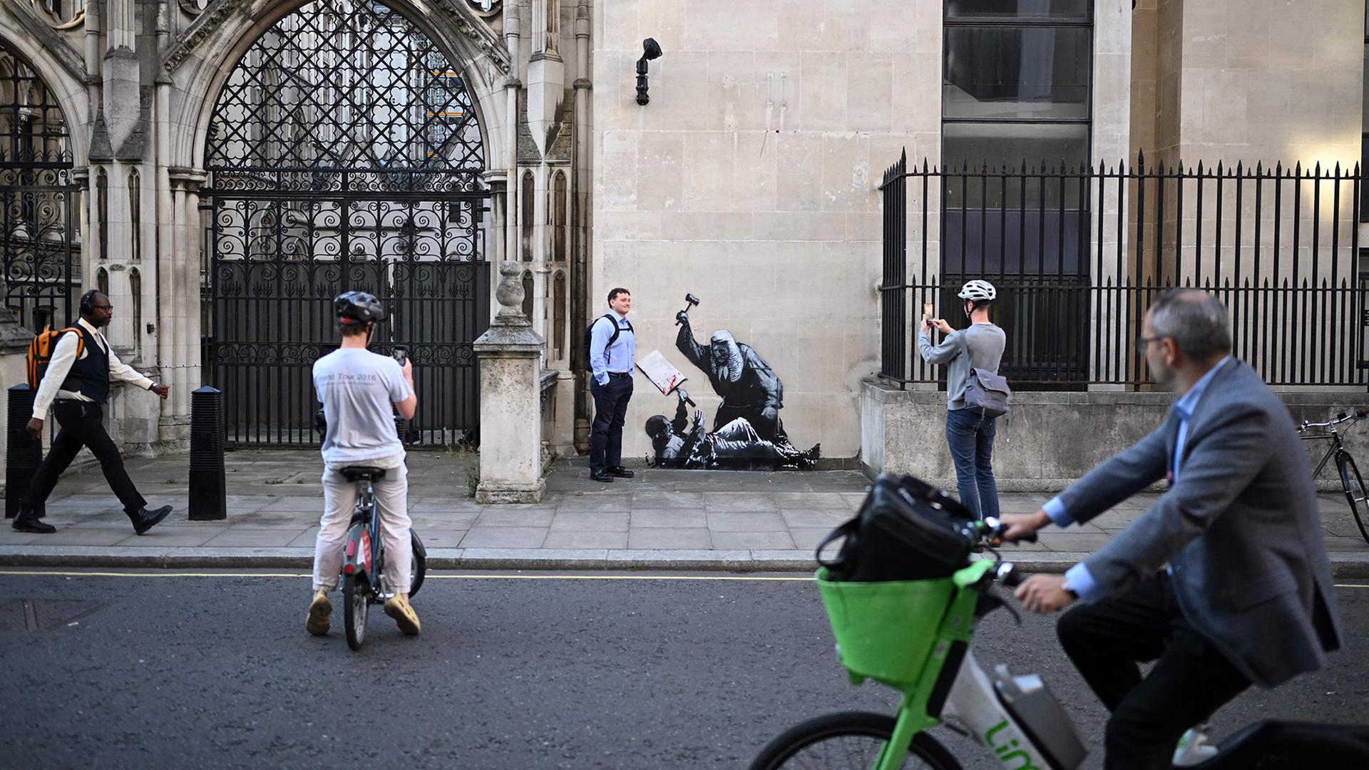 Menschen fotografieren ein Kunstwerk von Banksy an einem Gerichtsgebäude in London. | AFP
