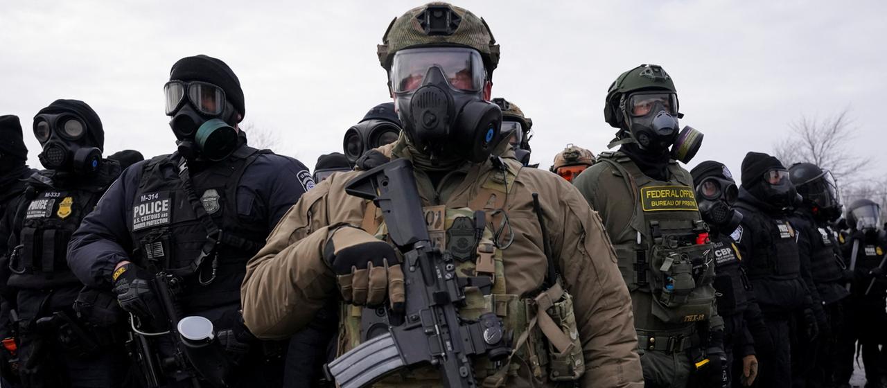 Schwer bewaffnete Männer in Uniform und mit Atemmasken über dem Gesicht