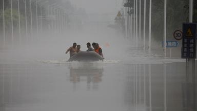 Männer fahren in einem Schlauchboot durch die völlig überfluteten Straßen der chinesischen Stadt Zhouzhou.