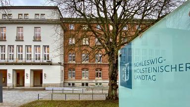 Ein großes Schild mit dem Schriftzug "Schleswig-Holsteinischer Landtag" steht vor dem Gebäude des Landeshauses in Kiel.