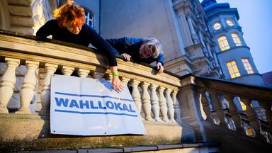  Zwei Wahlhelfer hängen am Wahllokal im Carl-von-Ossietzky-Gymnasium in Berlin-Pankow vor Wahlbeginn ein Hinweisschild auf. 