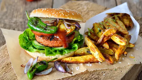 Burger végétalien avec galette soja-seitan, légumes grillés et pimientos, servi avec des frites.