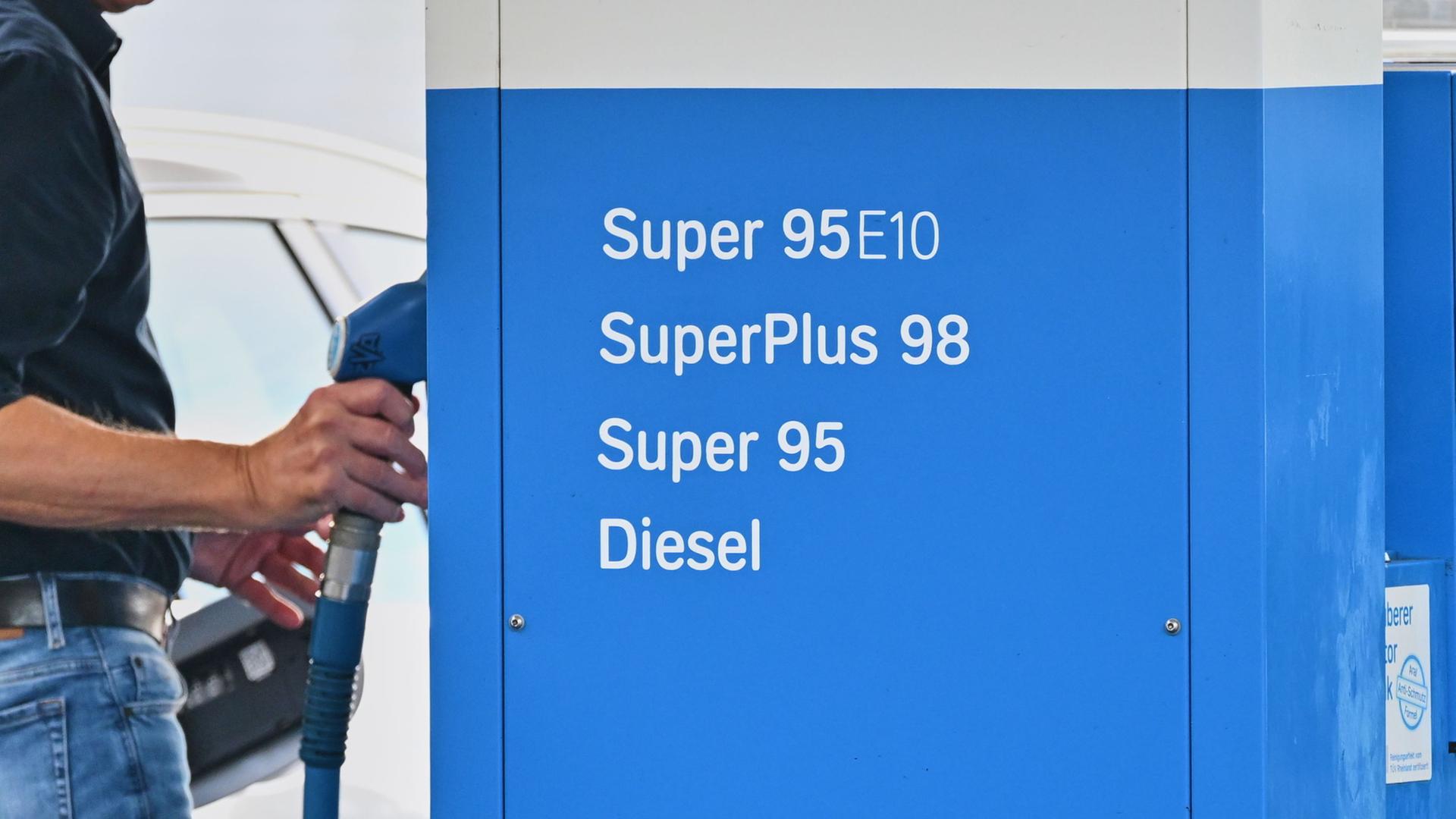 Ein Mann greift an einer Tankstelle nach einem Zapfhahn. | Sina Schuldt/dpa