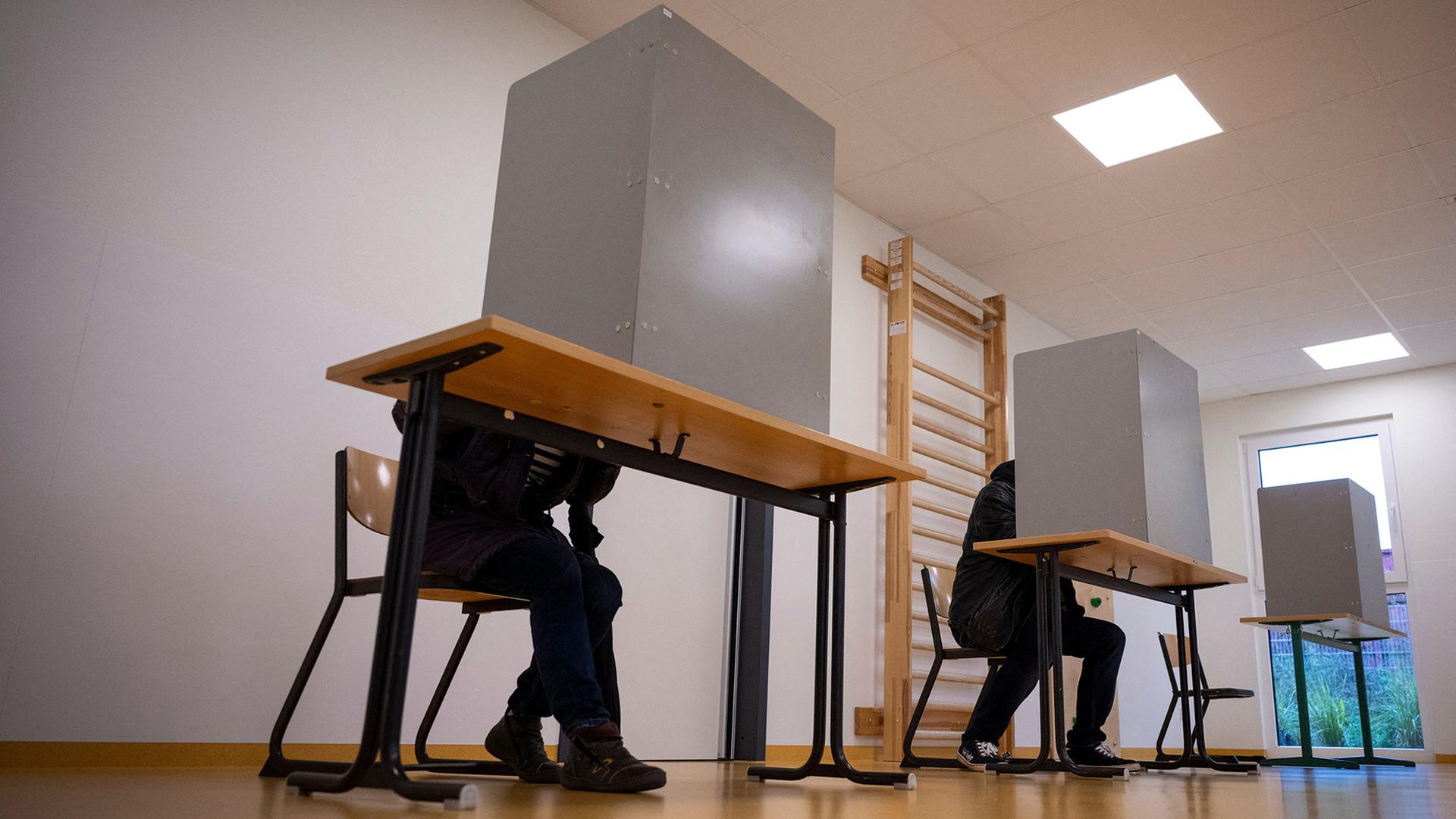 Die ersten Wähler sitzen am Morgen in einer Wahlkabine in Schwerin. | Philip Dulian/dpa