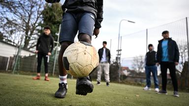 Ein Jugendlicher spielt Fußball mit anderen geflüchteten Jugendlichen.
