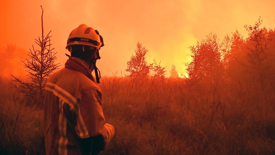 Feuerwehrmann in Schutzkleidung steht vor einem Brand