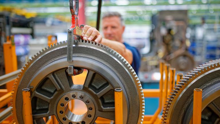 Ein Mitarbeiter befestigt bei Heidelberger Druckmaschinen ein Zahnrad an einem Lastkran.