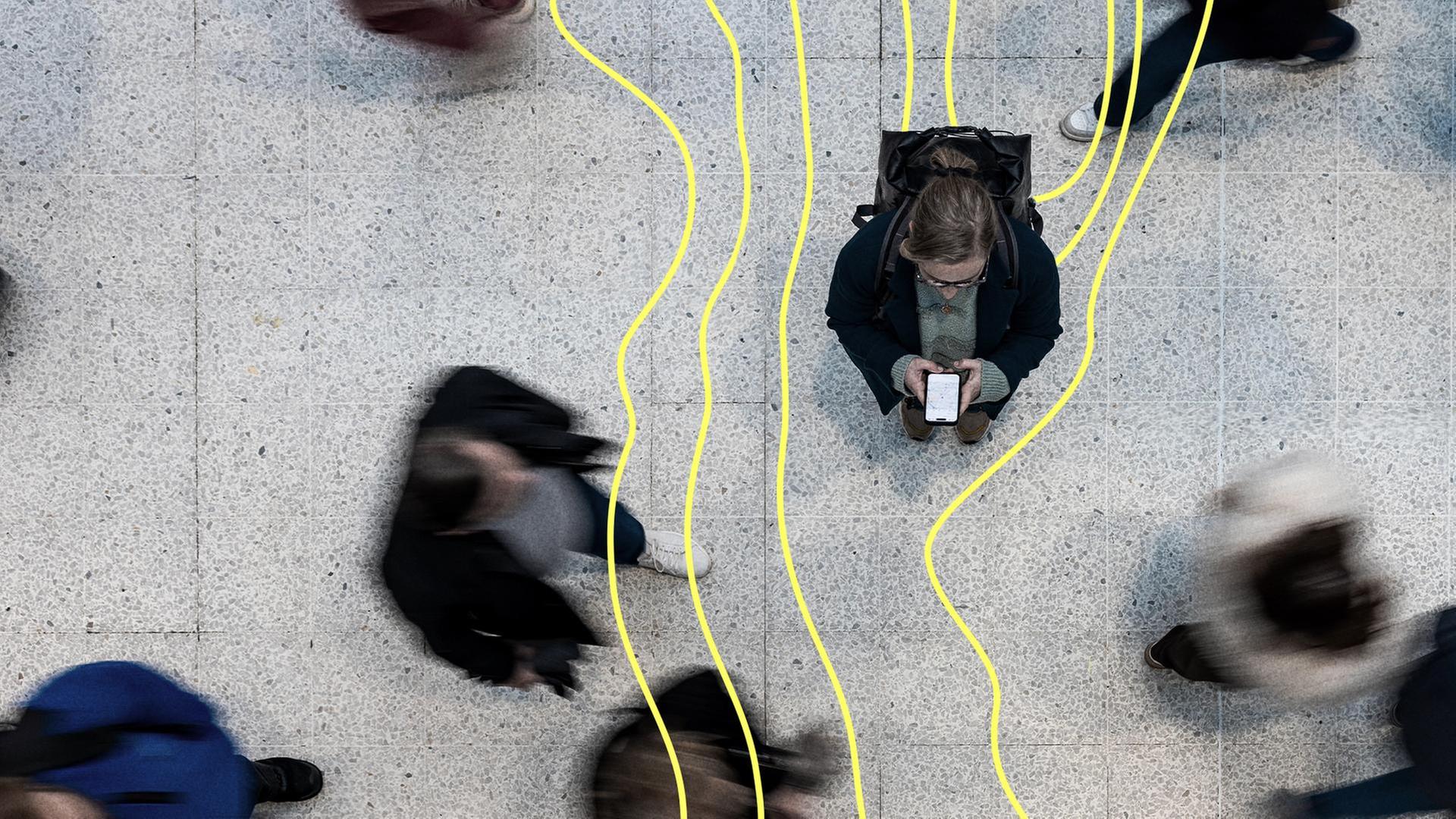 Eine Frau steht mit ihrem Handy in der Mitte wÃ¤hrend Passanten um sie herumgehen. | picture alliance / Westend61, William Perugini