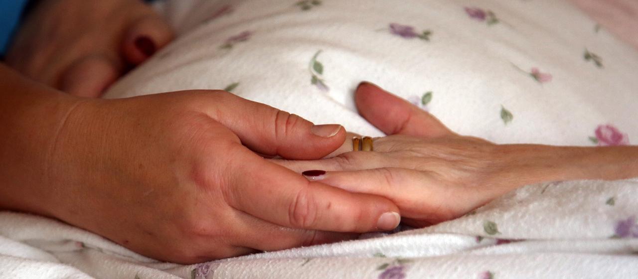Die Hände einer Bewohnerin liegen in einem Hospiz auf einer Bettdecke.