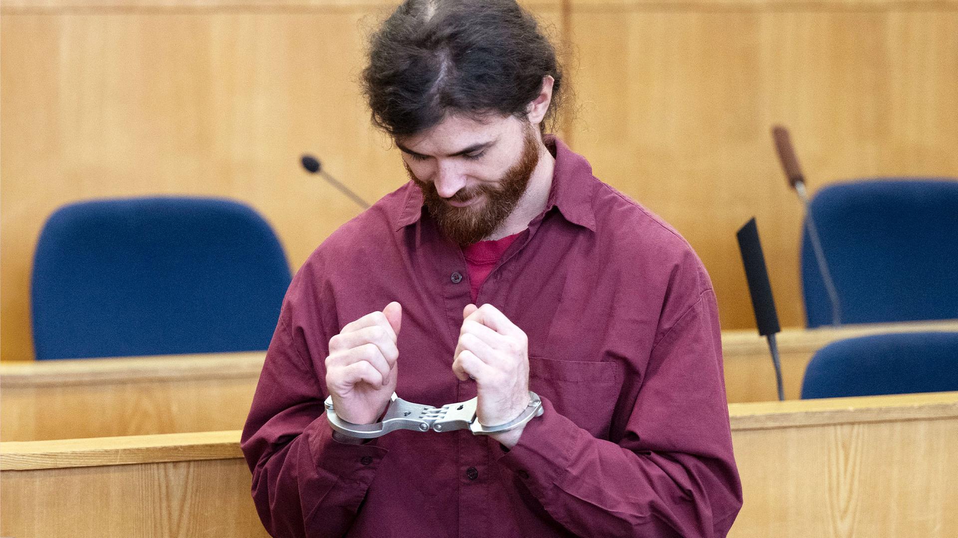 Franco A. senkt den Kopf und blickt auf die Handschellen an seinen Handgelenken. | picture-alliance/dpa