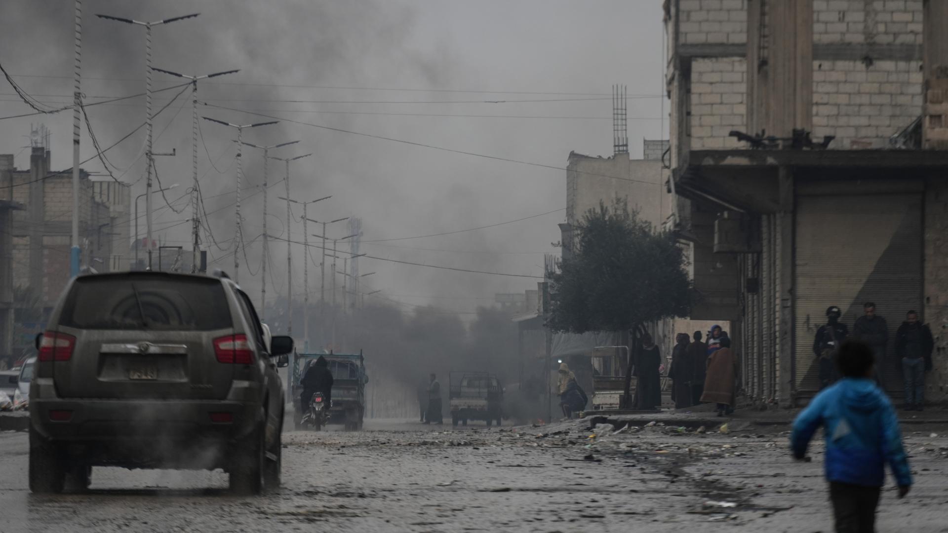 Eine Straße in Tabka in Syrien - im Hintergrund steigt dunkler Rauch. | dpa